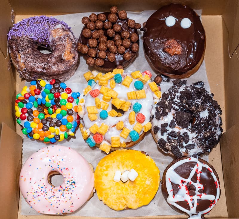A box of Naughti Donut limited-edition gourmet donuts, each finished in a different decadent glaze and topping